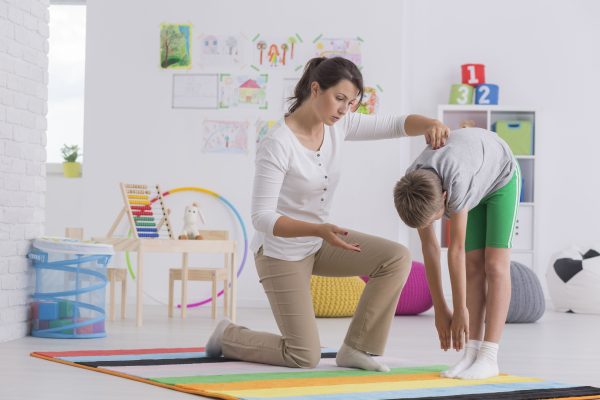 Child standing forward bend while exercising with physiotherapist